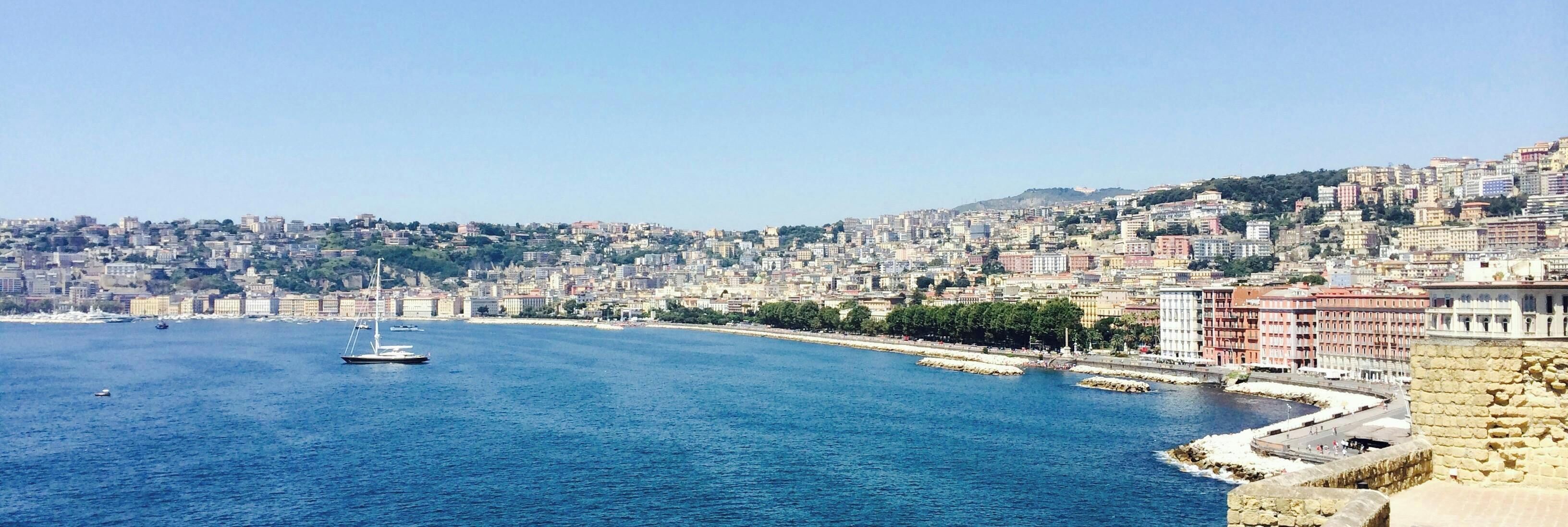 Paisagem costeira urbana com um porto, edifícios históricos e um muro de pedra.