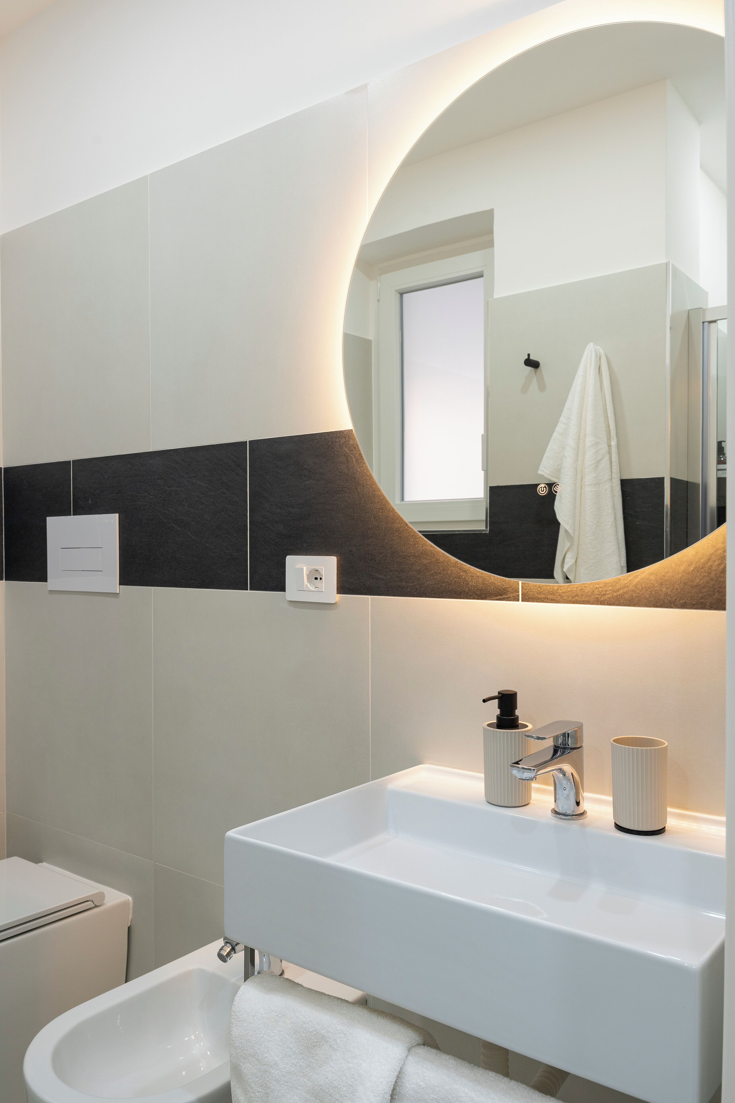 A modern bathroom with a large mirror, a white sink, a bidet, and a towel rack.