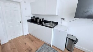 A compact kitchen with white cabinets, a black countertop, a small refrigerator, and a trash bin. - Studio Flat 2 in Golders Green (London)