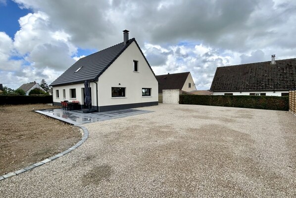 Une maison à deux étages avec un toit en pente, une terrasse couverte et une allée gravillonnée.