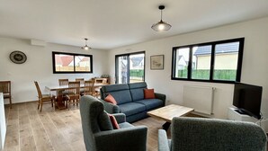 Ett vardagsrum med en soffa, fåtöljer, ett soffbord, en tv och en matplats med stolar och ett bord.