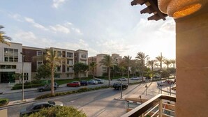 A residential area with modern apartment buildings, a road with cars, and palm trees.