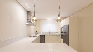 A modern kitchen with white countertops, a stainless steel range hood, a dishwasher, and a refrigerator.
