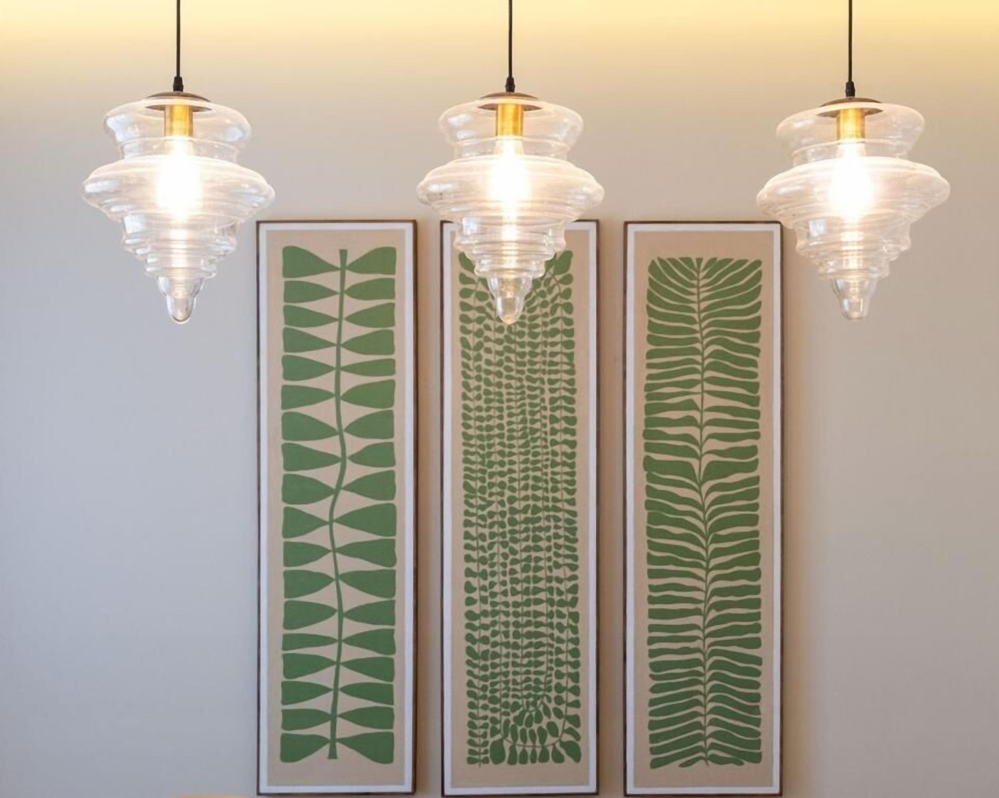 Três gravuras botânicas emolduradas numa parede, cada uma iluminada por uma luminária pendente.