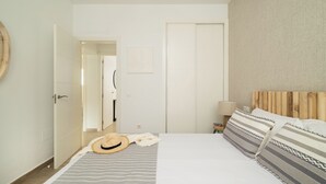 Un dormitorio con cama, cabecera de madera, manta a rayas, un sombrero y una almohada.