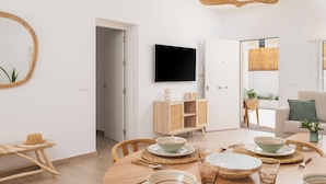 Una sala de estar moderna con comedor, un televisor de pantalla plana montado en la pared y una lámpara de techo de mimbre.