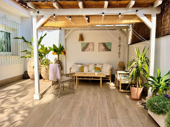 A cozy outdoor seating area with a wooden bench, a wicker chair, and a cushioned sofa under a wooden pergola.