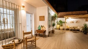 Un amplio espacio exterior con piso de madera, zona de estar con sillas, una mesa y plantas en macetas.