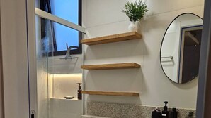 Un baño moderno con ducha de vidrio, inodoro, lavabo con encimera de granito y estantes de madera.