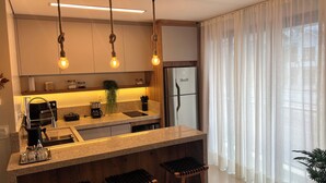 Una cocina moderna con horno empotrado, cafetera y refrigerador. Hay lámparas colgantes y una planta en la encimera.