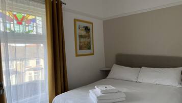A hotel room with a bed, a window with curtains, a framed picture on the wall, and a view of buildings outside.