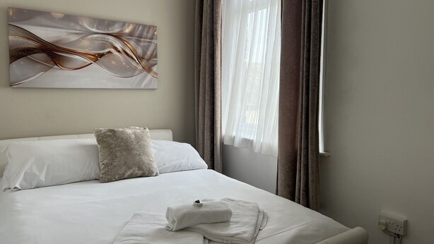 Habitación de hotel con cama, un cuadro abstracto colgado en la pared, una ventana con cortinas y una cama bien hecha con toallas.
