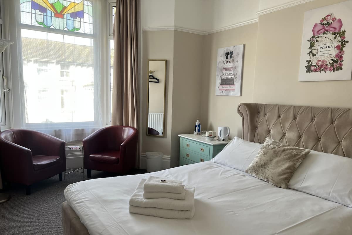 Habitación de hotel con cama, dos sillas, cómoda, espejo y ventana con cortinas.