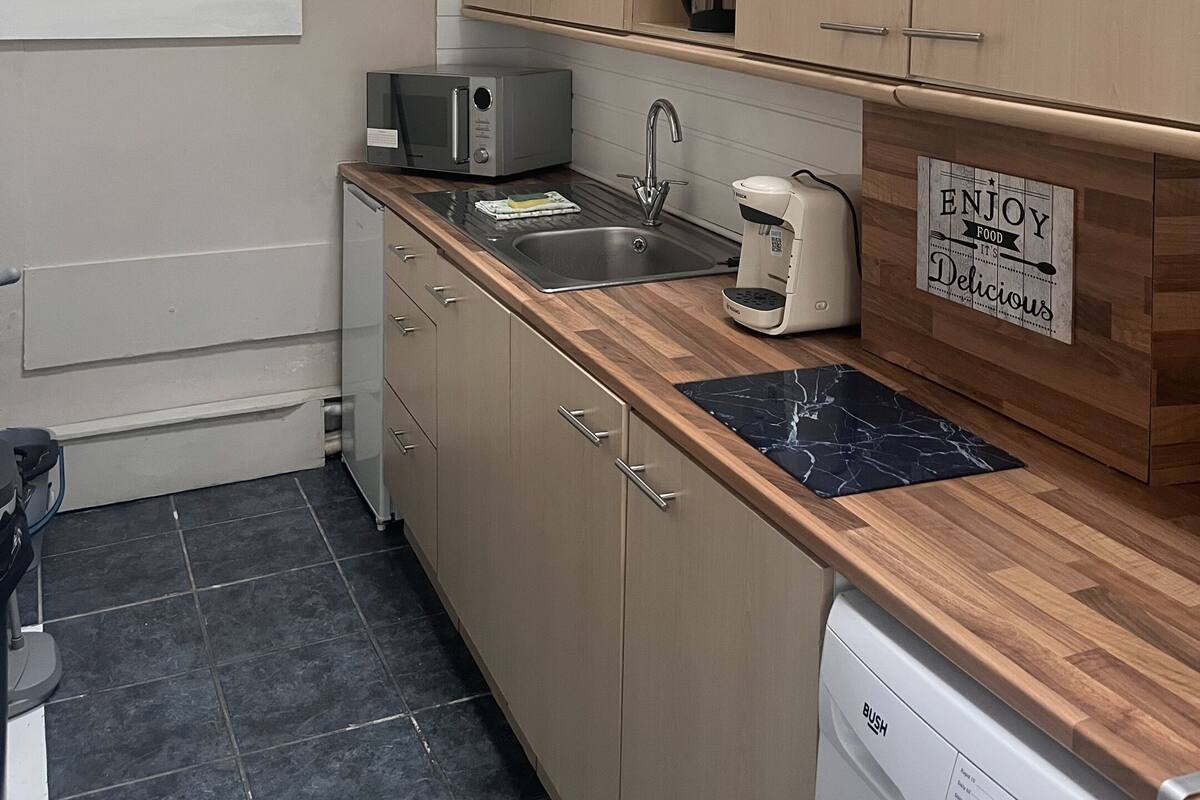 Una cocina moderna con armarios de madera, microondas integrado, pileta y cafetera.
