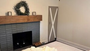 A bedroom with a fireplace, a bed with a white blanket, a ceiling fan, and a door with a white X design. - Adorable 2-bedroom Farmhouse in beautiful Lake Guntersville (Guntersville)