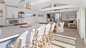 Une cuisine spacieuse avec des meubles blancs, un grand îlot central doté de chaises en osier et un coin repas avec un canapé et une table.