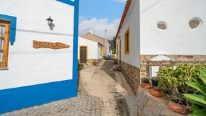 A narrow cobblestone street flanked by white buildings with blue trim and yellow doors, leading to a distant building with a visible sign. - Villa 'Terra' with Private Terrace, Shared Garden and Wi-Fi (Monchique)
