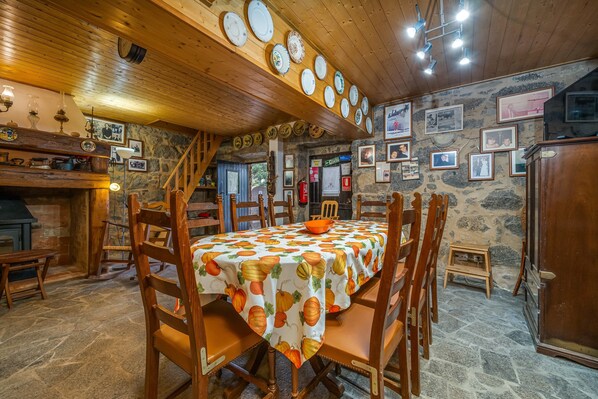 Comedor rústico con pared de piedra, techo de madera y una mesa cubierta con mantel de motivos de calabaza.