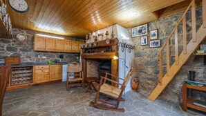 A rustic kitchen with wooden cabinets, a stone floor, a wooden rocking chair, and a staircase. - Villa 'Terra' with Private Terrace, Shared Garden and Wi-Fi (Monchique)