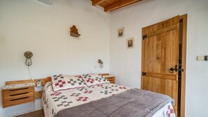 A bedroom with a wooden bed, bedside tables, a nightstand, a wooden door, and a wall-mounted light fixture.