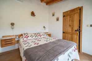 Une chambre à coucher avec un lit en bois, des tables de chevet, une petite table de nuit, une porte en bois et un luminaire fixé au mur.