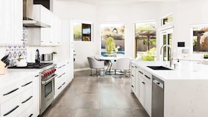 Una cocina moderna con armarios blancos, horno empotrado y comedor con mesa y sillas.