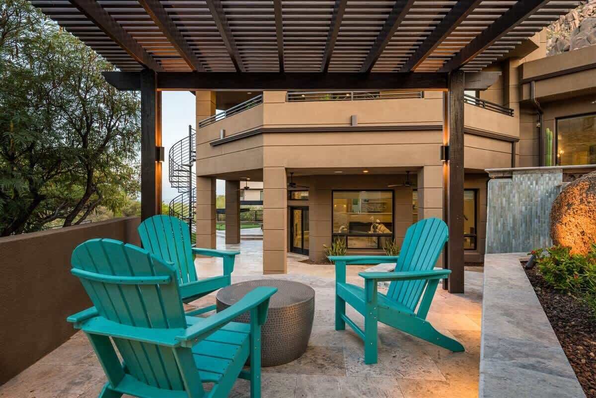 An outdoor patio with Adirondack chairs, a round table, and a pergola structure.