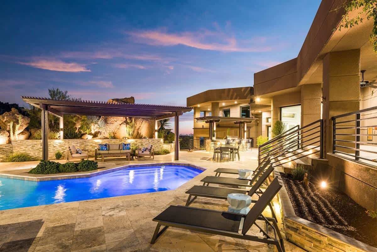 Una piscina con sillas de descanso, una pérgola y un muro de piedra.