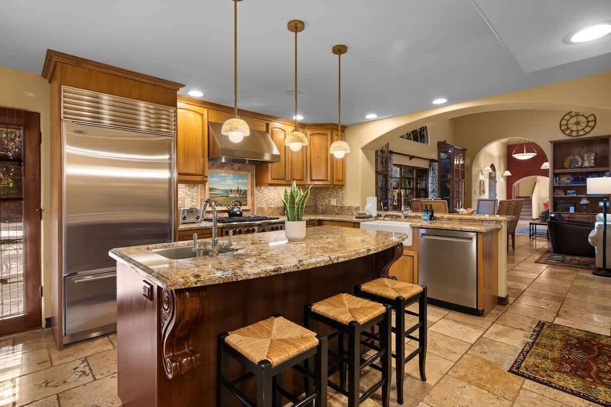 A spacious kitchen with a large island, stainless steel appliances, wooden cabinets, and pendant lighting.
