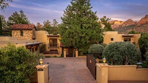 A gated entrance to a property with a paved driveway, a stone building, and a large tree.
