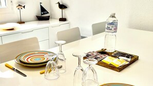 Una mesa de comedor dispuesta con platos de colores, copas de vino, cubiertos y una botella de agua.