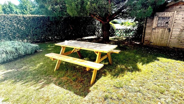 Una mesa de picnic en un área con césped, un árbol y una estructura de madera al fondo.