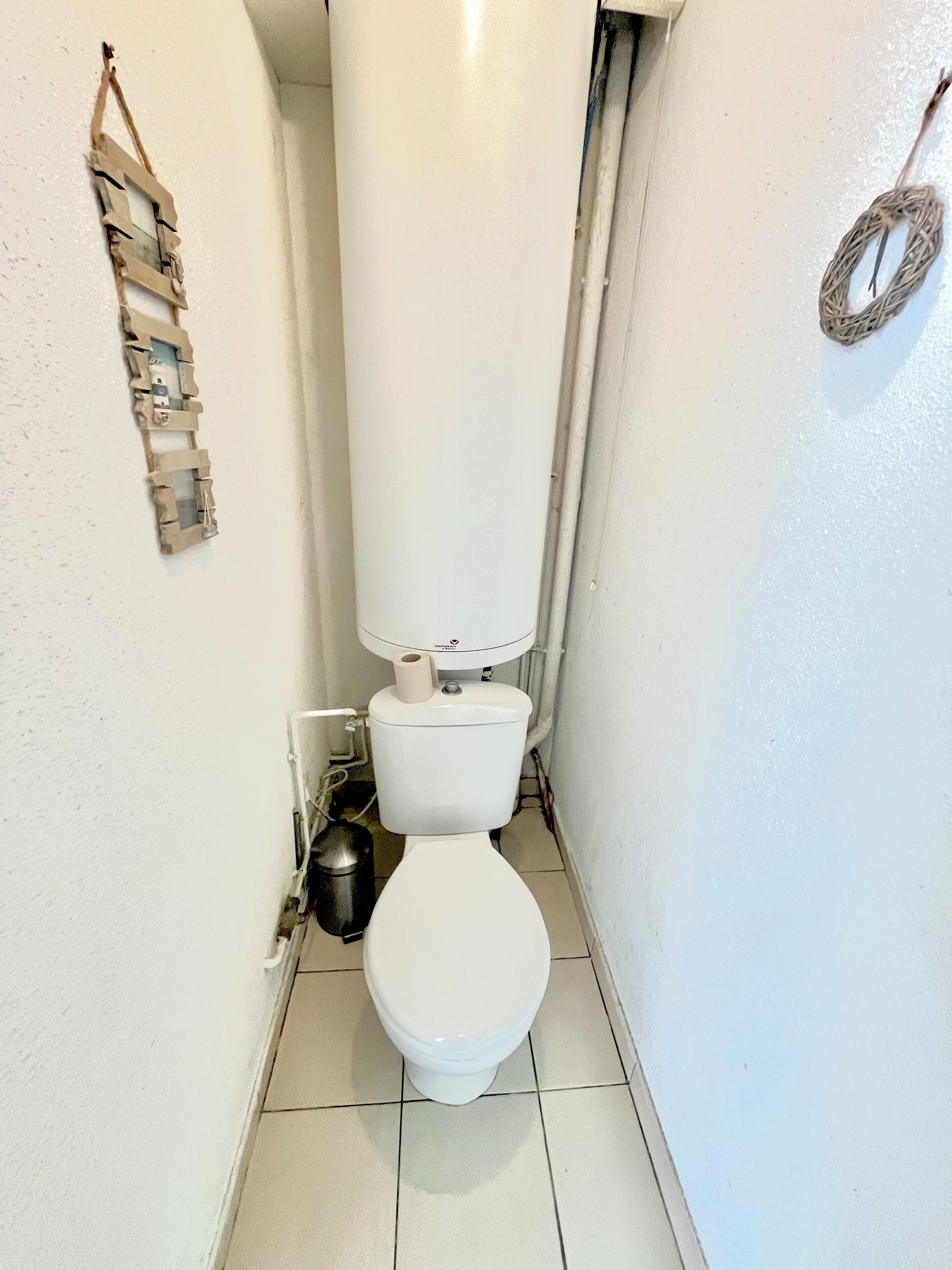 A small, narrow bathroom with a white toilet, a trash bin, and a toilet paper holder.
