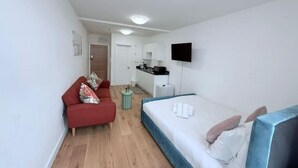 Ett modernt hotellrum med en röd soffa, en säng med blått huvudgavel, ett litet runt bord och en tv som är monterad på väggen.