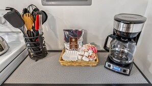 A kitchenette with a coffee maker, a basket of utensils, and a package of coffee pods. - Merlot Cottage - GOTL Strip - Lover's Retreat (Geneva)