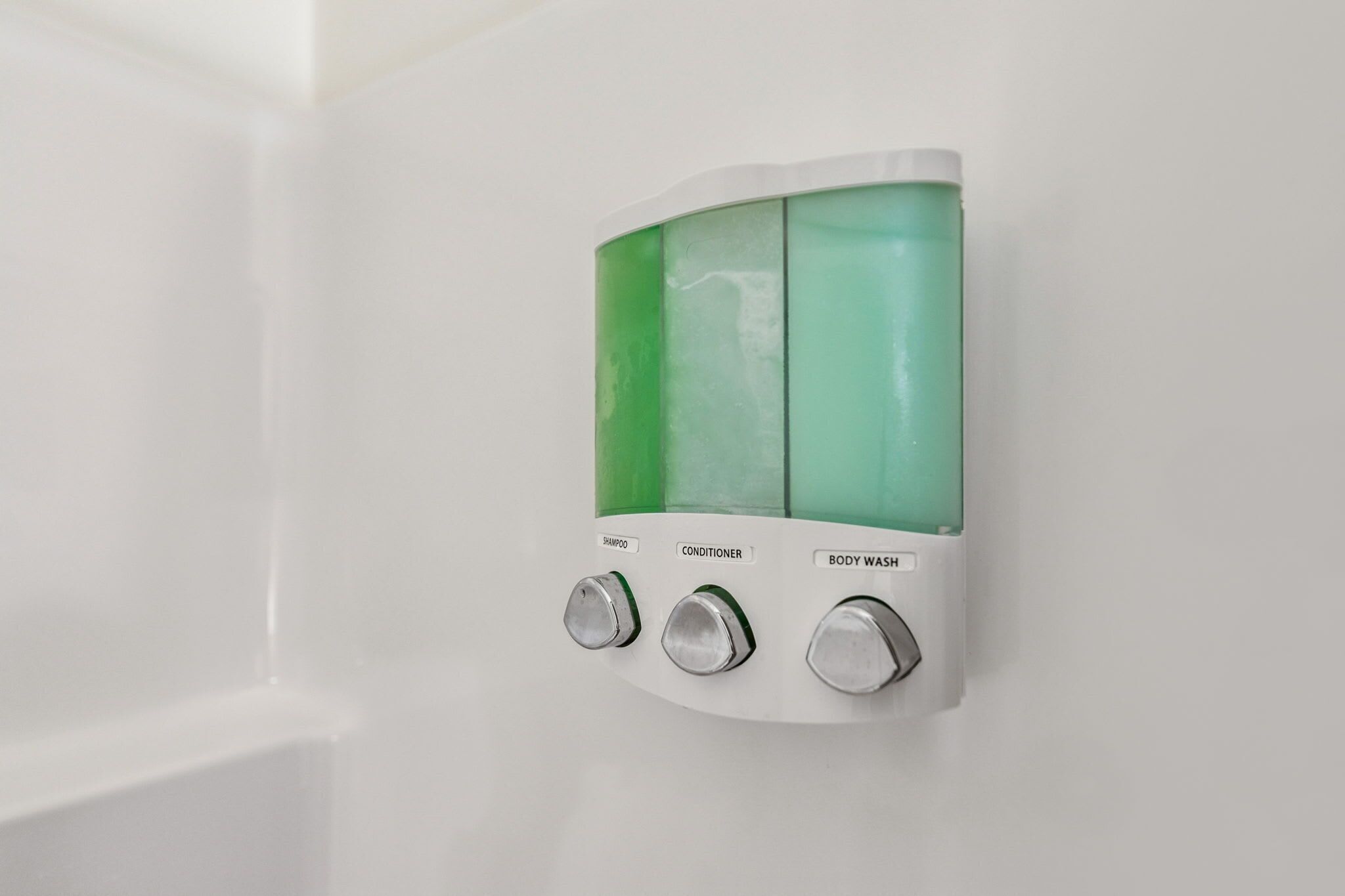 A wall-mounted dispenser with three compartments labeled shampoo, conditioner, and body wash.