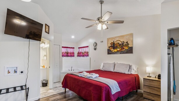 A bedroom with a large bed, a ceiling fan, a TV, and a painting on the wall. - Merlot Cottage - GOTL Strip - Lover's Retreat (Geneva)