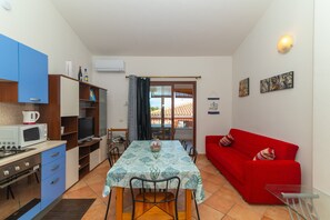 A compact living space with a dining table, red sofa, kitchenette, and a view through a glass door. - Apartment 'Posada' with Sea View, Wi-Fi and Air Conditioning (Posada)
