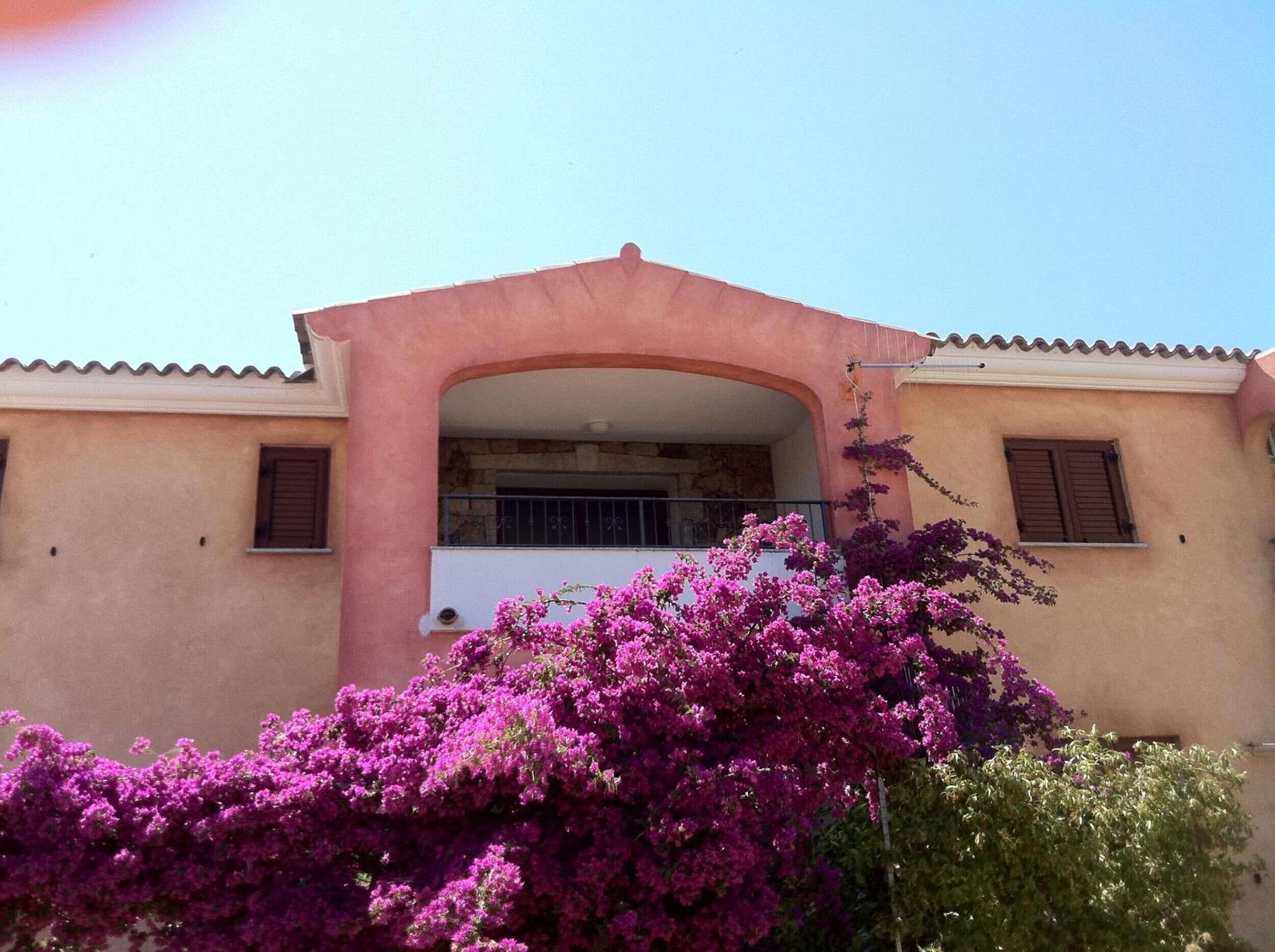 A building with a balcony, a stone wall, and pink bougainvillea flowers.