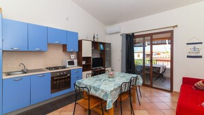 Une cuisine de taille réduite avec des meubles bleus, une table à manger avec des chaises, un canapé rouge et une porte-fenêtre coulissante donnant sur un espace extérieur.