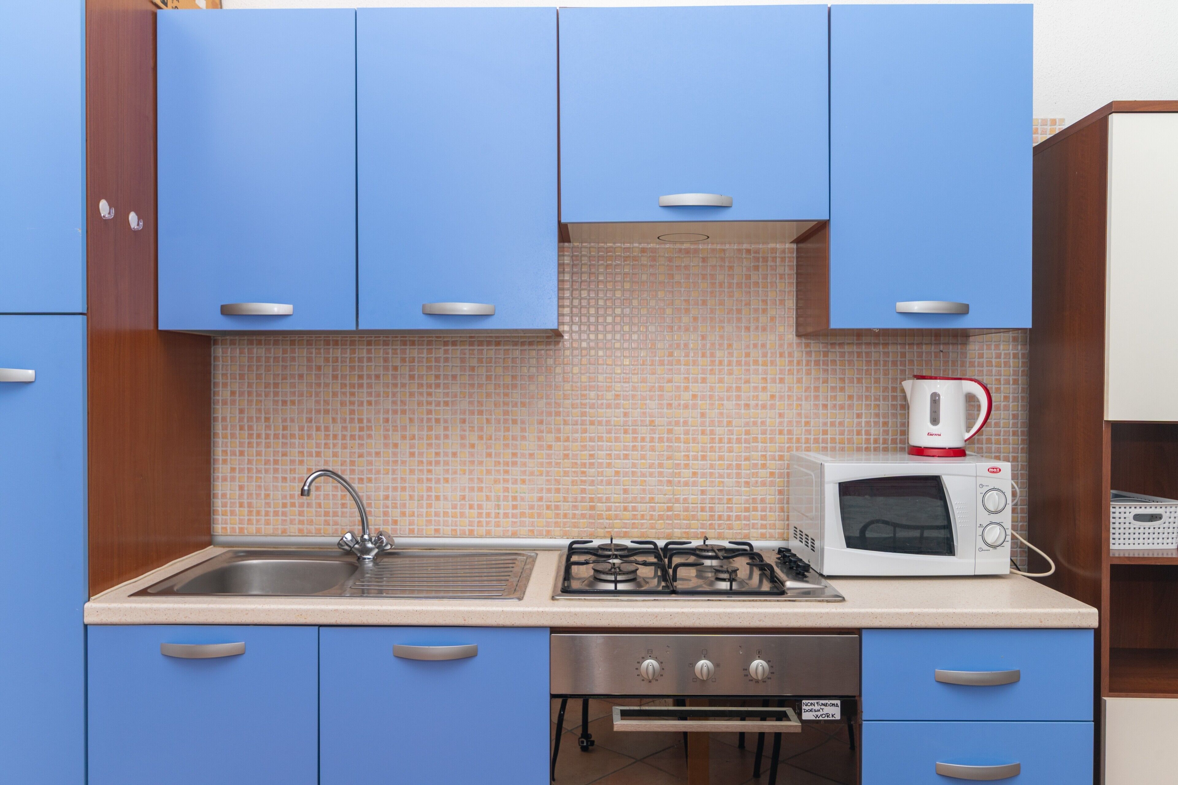 A kitchen with blue cabinets, a gas stove, a microwave, and a sink.