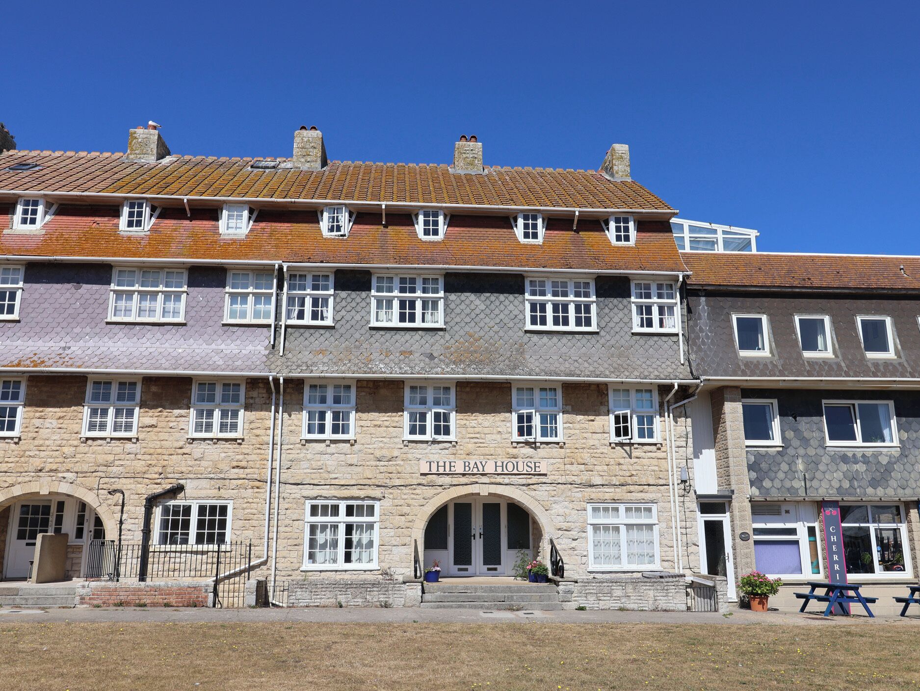 A multi-story building with a stone facade, a sign reading 'THE BAY HOUSE,' and a small entrance with steps.