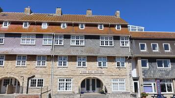 A multi-story building with a stone facade, a sign reading 'THE BAY HOUSE,' and a small entrance with steps.