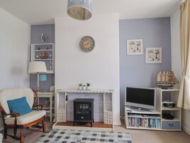 A living room with a fireplace, a television, a bookshelf, and a clock on the wall.