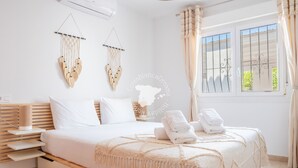 Un dormitorio moderno con cama, mesitas de noche, un adorno de macramé en la pared y una ventana con cortinas.