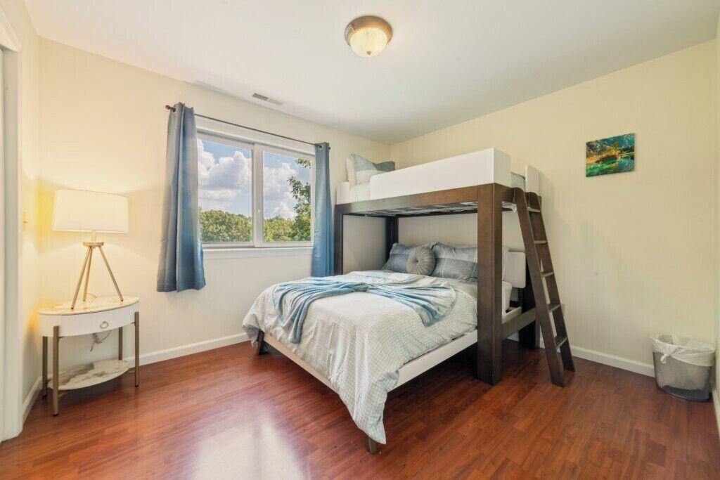 A bunk bed room with a window, a bedside lamp, and a small table.