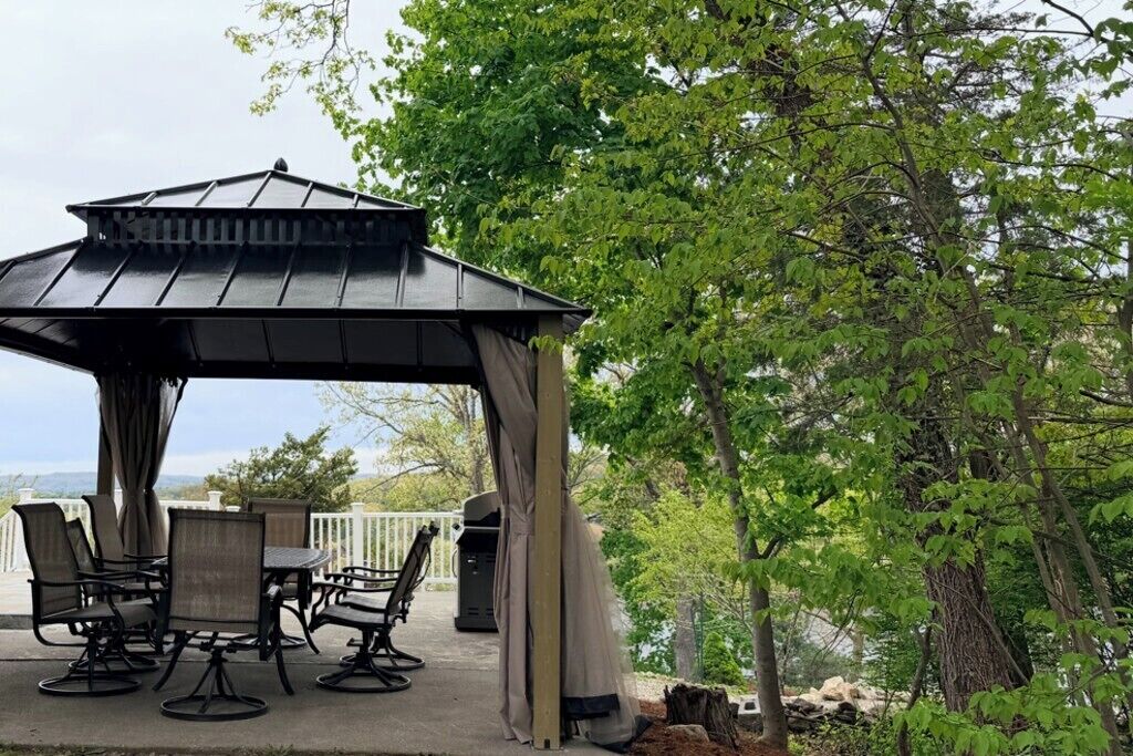 Um gazebo com mesa e cadeiras, rodeado por árvores.