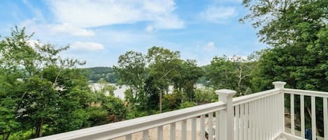 A wooden deck with white railings overlooking a lake and trees.