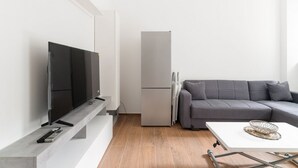 A modern living room with a flat-screen TV, a grey sofa, a white coffee table, and a built-in grey refrigerator. - GuestHost - Cozy 55 sqm apartment, perfect for 3 people, located on the second floor of a building with an elevator (NOT accessible to disabled guests).The property is located in the Corvetto neighborhood, in a quiet residential area just steps from Vett (Milan)