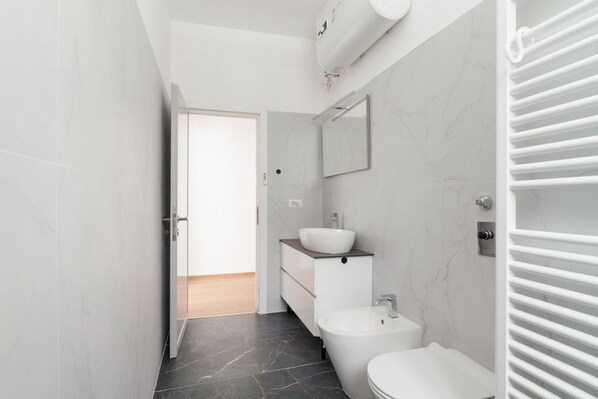 A modern bathroom with a toilet, bidet, and sink, marble walls, and a towel rack.